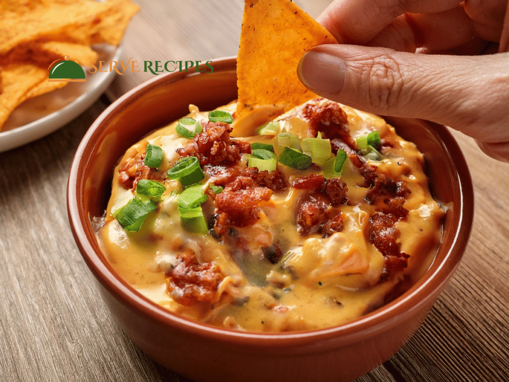 Buffalo chicken dip with melted cheese and green onions, being dipped with a tortilla chip, served in a brown bowl.