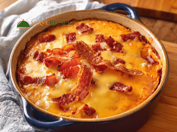 Spicy buffalo chicken dip in a blue ceramic dish, topped with melted cheese and crispy bacon pieces.