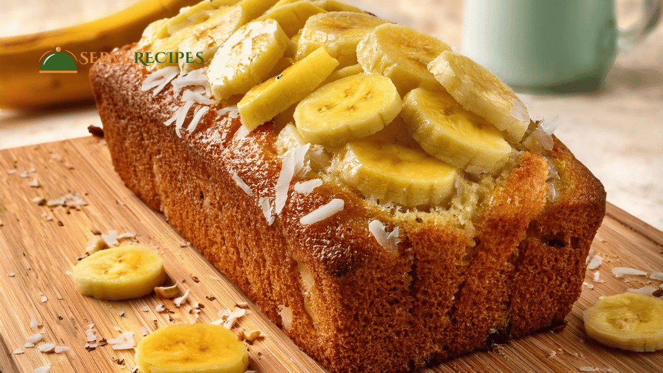 A loaf of Banana Bread with a Tropical Twist, featuring visible chunks of pineapple and shredded coconut, served on a white plate.