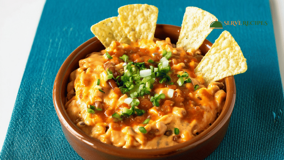 Creamy Buffalo Chicken Queso Dip garnished with green onions, served with blue corn tortilla chips, celery, and carrot sticks on a wooden table.