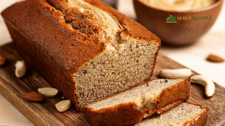 A freshly baked loaf of healthy banana bread with visible chunks of banana, sliced on a wooden board.